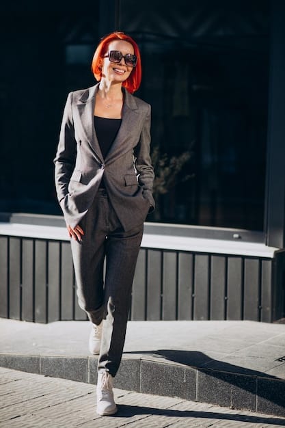 A woman wearing an oversized blazer paired with tailored pants and sneakers, creating a modern and chic K-drama-inspired look. She is walking down a city street with a stylish coffee shop in the background.