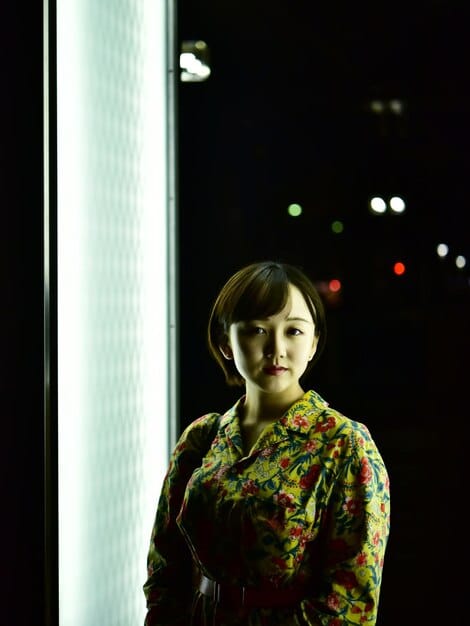 A medium shot from a Korean drama showcases dramatic lighting, with one side of an actor's face brightly lit and the other side shrouded in deep shadow. This chiaroscuro effect emphasizes the internal conflict and emotional depth of the character. Background is dark and out of focus.