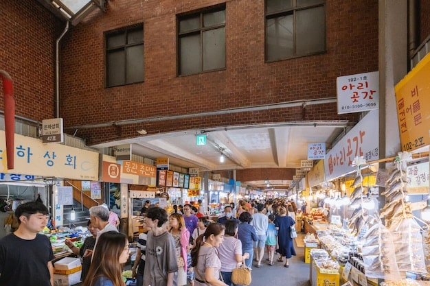 A bustling street food market in Seoul, South Korea. Various stalls are visible, showcasing popular street foods like tteokbokki, Korean fried chicken, and hotteok. The scene captures the energetic atmosphere and diverse culinary offerings.