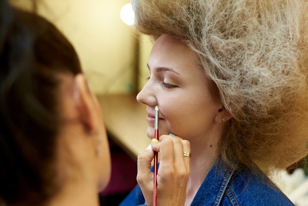 A makeup artist using an airbrush to apply foundation on an actress's face. The focus is on the even, flawless finish achieved through this technique, highlighting its importance in HD filming.