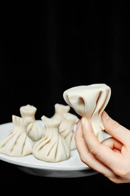 A close-up shot of a hand skillfully crafting delicate dumplings, showcasing the intricate folds and precise technique. The background is slightly blurred, drawing focus to the dumpling being made and the artisan's hand. The lighting is soft and even, highlighting the textures of the dough and the filling.