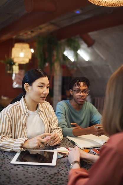 A group of diverse people sitting around a table, animatedly discussing a Japanese drama episode, with laptops and phones scattered around them, indicating their engagement in online forums and social media.