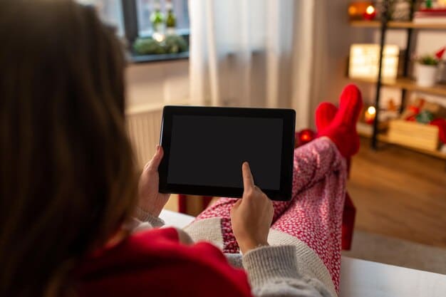 A tablet displaying the Tubi interface, showcasing a variety of movie thumbnails. The tablet is held by a hand, with a blurred background of a cozy living room.